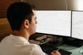 Successful young trader in casual wear working with charts and market reports at home