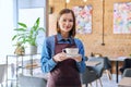 Young woman worker, owner in apron holding cup of coffee in restaurant, coffee shop Royalty Free Stock Photo