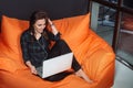 Successful young woman sitting on sofa in office, working on her laptop. Royalty Free Stock Photo