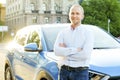 Successfull happy young man and his car in soft sunset light on urbanistic background. Busines man with vehicle on roadside. Royalty Free Stock Photo