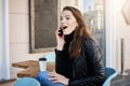 Such great news. Portrait of impressed and excited young european female in stylish outfit sitting in cafe, drinking