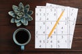 Sudoku, pencil, cup of coffee and decorative succulent on wooden table, flat lay