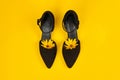 Suede black court shoes with yellow Topinambur flower bud inside toe, yellow background, womanhood