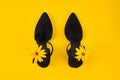 Suede black court shoes with yellow Topinambur flower bud on strap, yellow background, trendy shoes