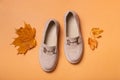 Suede woman's shoes with autumn leaves on orange background flat lay, top view.