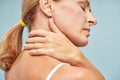 Suffering from back pain. Rear view of a mature woman touching her neck while standing against blue background Royalty Free Stock Photo