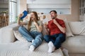 Suffering from heat family couple sitting on couch waving paper fans at home. Royalty Free Stock Photo