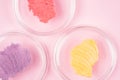 Sugar body scrub smears texture. Pink red, purple and yellow scrub smudges in petri glass dishes over pastel pink background