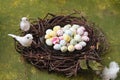 Sugar candy in the form of bird eggs on a glass plate in a wreath of branches on a green concrete background. Spring equinox day,