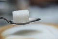 Sugar cube balanced on a spoon above smooth white surface Royalty Free Stock Photo
