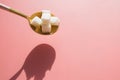 Sugar cubes in golden metal spoon on pink background