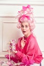 Portrait of charming young girl, princess wearing pink wig and eating candies, sweets over luxury interior background Royalty Free Stock Photo