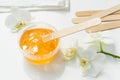 Sugar paste or wax honey in a transparent jar and white orchid on a white background. Sugaring. Depilation and beauty