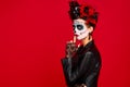 Sugar skull pretty girl with halloween makeup standing on bright red background. Wonderful female zombie with flowers in hair