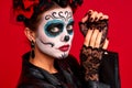 Sugar skull pretty girl with halloween makeup standing on bright red background. Wonderful female zombie with flowers in hair