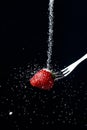 Sugar sprinkles on fresh ripe red strawberry with fork on black background Royalty Free Stock Photo