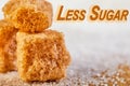 Less sugar text. Cubes of yellow sugar lying on a background of white sugar. Diet and health concepts