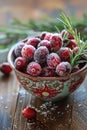 Sugared cranberries in decorative bowl with rosemary sprigs on wooden table