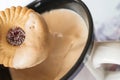 Sugared jam ring biscuit being dunked into frothy coffee in a mug