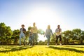 Suggestive low angle view of group of young multiracial gen-z friends running on green field with setting sun at their back with Royalty Free Stock Photo