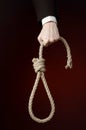 Suicide and business topic: Hand of a businessman in a black jacket holding a loop of rope for hanging on dark red isolated