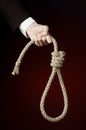 Suicide and business topic: Hand of a businessman in a black jacket holding a loop of rope for hanging on dark red isolated