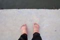 Female barefoot standing on hard cement pathway with dark river below Royalty Free Stock Photo