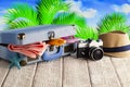 Suitcase full of holiday items - photo camera, summer hat, tanning oil, towel and flip flops on tropical background Royalty Free Stock Photo