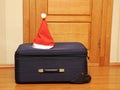 Suitcase and santa hat against a wooden door. Royalty Free Stock Photo