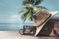 Suitcase, sun hat, photo camera and sunglasses with sea water, coconut palm tree and blue sky background on sunny summer day in Royalty Free Stock Photo