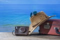 Suitcase, sun hat, photo camera and sunglasses on wooden deck with sea water background on sunny summer day in tropical beach, Royalty Free Stock Photo
