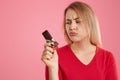 Sullen Caucasian young woman holds sweet, purses lip, has light hair, dressed in red jumper, isolated over pink background with