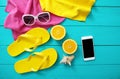 Summer accessories on blue wooden background. Yellow flip flops, towels, sunglasses, mobile phone and oranges. Mock up and top vie