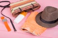 Summer accessories - straw beach bag, sun hat, belt, watch, suntan lotion, orange denim shorts on pink wooden table Royalty Free Stock Photo