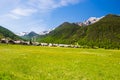 Summer in the Alps, tourist resort, vacation village. Blooming alpine meadow and lush green woodland set amid high altitude mounta Royalty Free Stock Photo