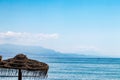 Summer backdrop. Selective focus is directed on a brown straw umbrella or beach parasol against blurred blue sea, mountains and Royalty Free Stock Photo