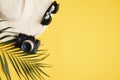 Summer background with beach hat, hipster sunglasses, retro style camera, tropical palm leaf on yellow. Flat lay, top view, copy