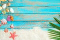 Summer background with beach sand, starfishs coconut leaves and shells decoration hanging on blue wooden background.