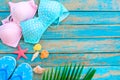 Summer background with bikinis, slippers, starfish, shells and coconut leaves on blue wooden background.