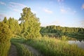Summer background - field road among meadows along the river bank. Sunset light. Plain landscape, Russia