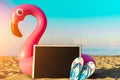 Summer background. Pink inflatable flamingo with black desk, slippers for text on summer sea beach background in sunny day. Trendy Royalty Free Stock Photo