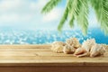 Summer background with wooden table, seashells and palm tree over sea bokeh Royalty Free Stock Photo