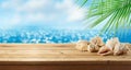 Summer background with wooden table, seashells and palm tree over sea beach bokeh. Tropical vacation concept Royalty Free Stock Photo