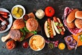 Summer BBQ food table with hot dog and hamburger buffet, flat lay over a dark background