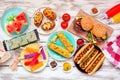 Summer BBQ food table scene with hamburgers and hot dogs over white wood