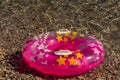 Summer beach composition. Pink inflatable float with stars on pebble, shingle, boulder sea background, trendy summer sea concept