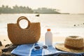 Straw bag, white sunglasses rest on blue striped towel at sunny sea shore. Summer beach day essentials hat, sunscreen Royalty Free Stock Photo