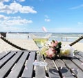 Summer beach romantic flowers a bouquet , glass of wine on wooden table,in air flying pink petal view to sea at horizon blue sk