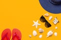 Summer beach sea accessories. Coral flip flops, blue straw hat, sunglasses, shells, starfish on yellow background top view flat Royalty Free Stock Photo