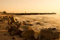 Summer, beach sunset by the sea. In the background, a breakwater from which people jump into the ram. On front huge stones, surf. Royalty Free Stock Photo